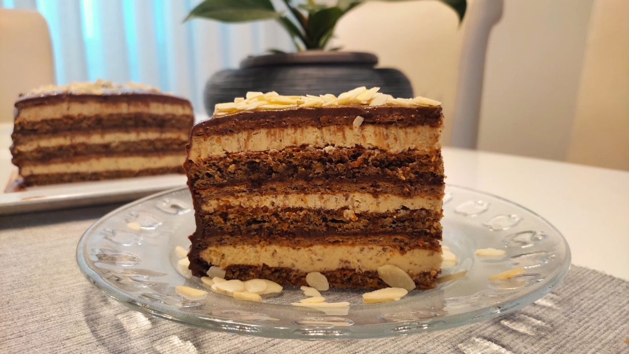 Slojevita tortica sa bademom i kremom prekrivena tamnom čokoladom, servirana na tanjiru