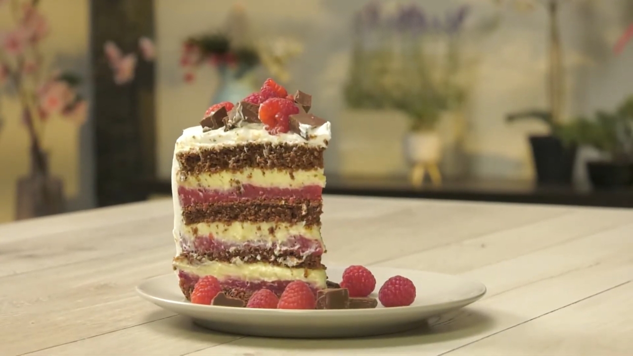 Parče uskršnje torte sa malinama i kremom, slojevito isečeno i servirano na tanjiru uz sveže maline