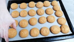 Pečeni medenjaci zlatne boje hlade se na plehu dok ih ruka pažljivo dodiruje da proveri mekoću