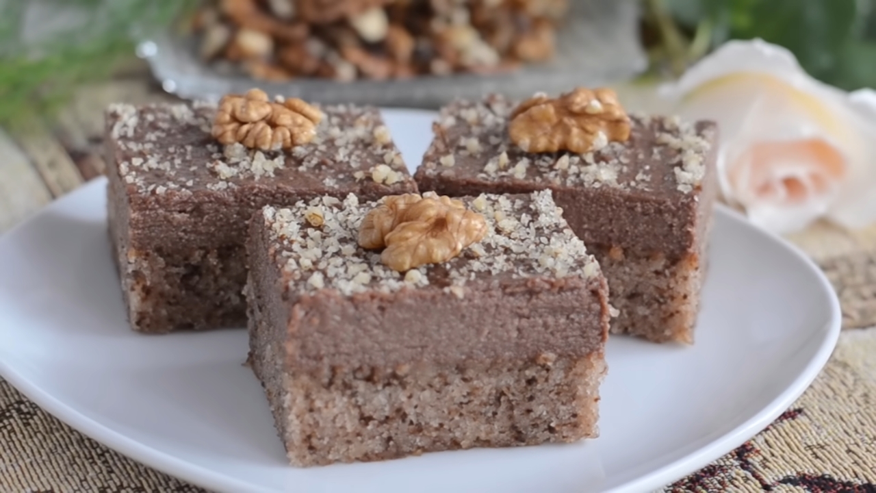 Kocke kolača sa orasima i čokoladom servirane na tanjiru, posute orasima i ukrašene polovinama jezgra
