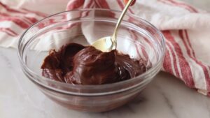 Gust čokoladni ganaš stoji u činiji dok ga kašika lagano zahvata