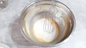 Metalna činija sa delimično umućenom smesom od otopljenog maslaca, šećera i meda, u koju je dodat beli šećer ili mleko