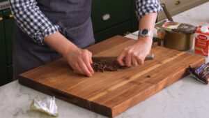 Osoba seče čokoladu na drvenoj dasci u kuhinji