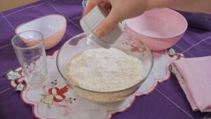 Ruka sipa brašno u činiju dok se priprema smesa za koru kolača sa orasima i čokoladom