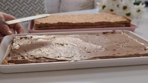 Na tacni se ravnomerno razmazuje čokoladni fil preko kore dok se priprema sledeći sloj torte